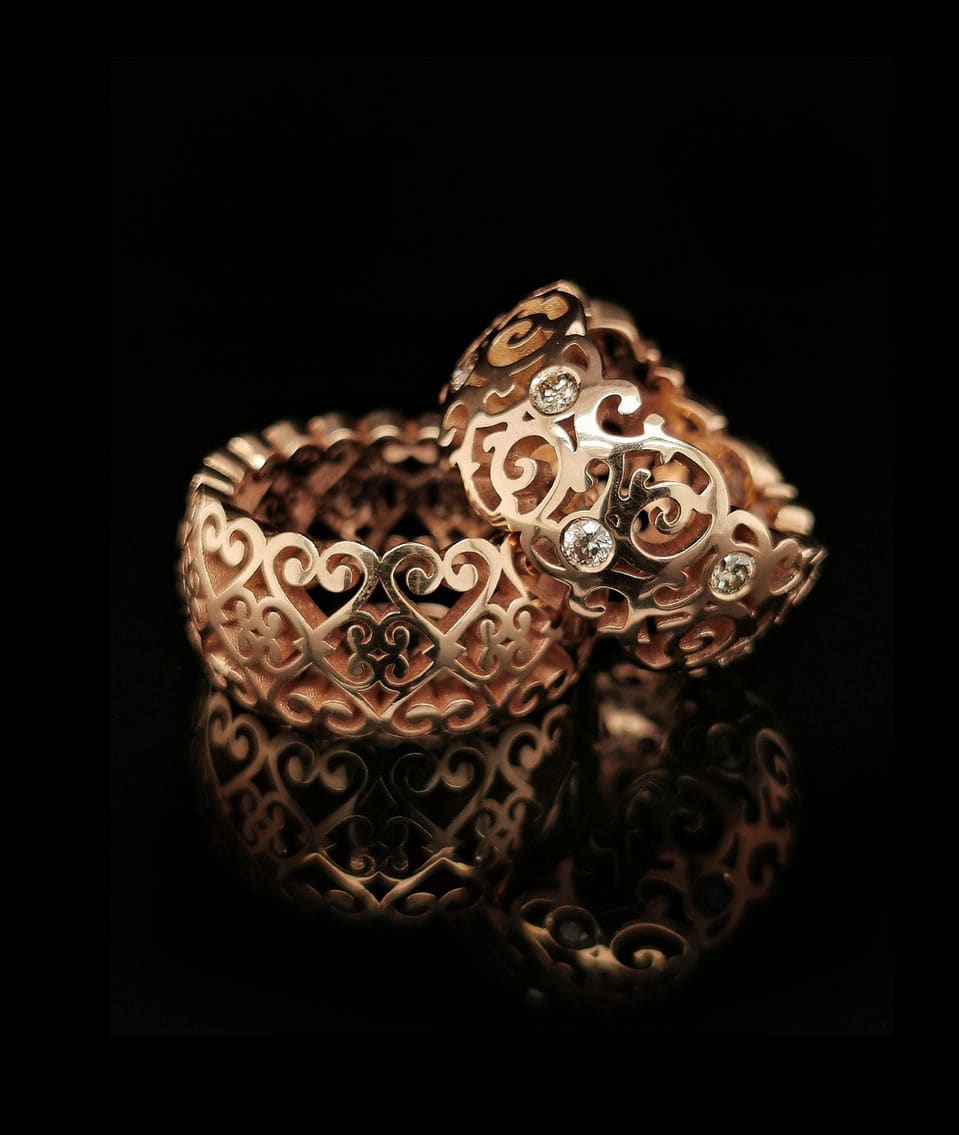 Twee rosé gouden ringen met hartvormig krulwerk en diamanten.